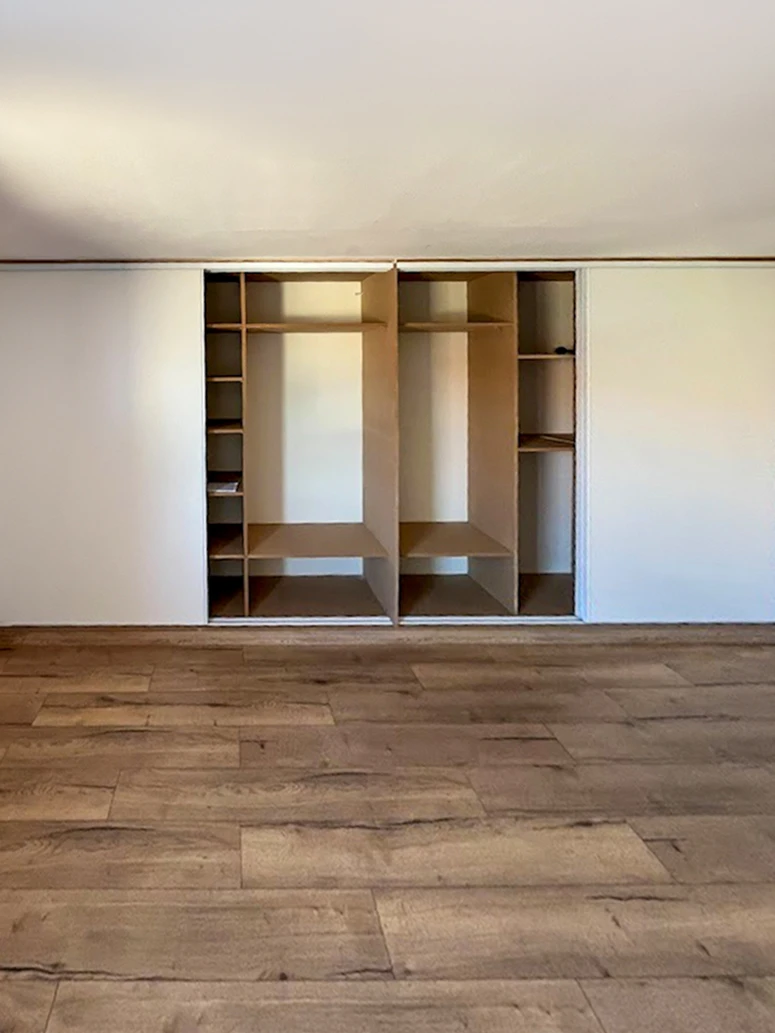 Chambre moderne avec dressing ouvert intégré au mur, présentant vêtements suspendus sur deux niveaux et chaussures rangées