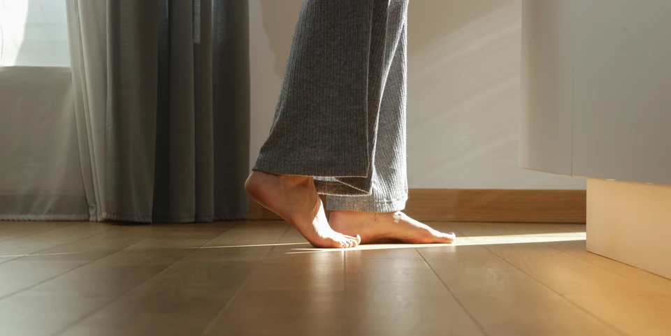 Intérieur moderne avec personne en pantalon de jogging gris marchant pieds nus sur parquet, près d'un canapé gris et d'un tapis blanc