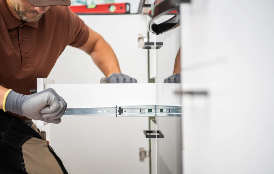 Cuisine moderne avec installateur professionnel en uniforme rouge montant un tiroir blanc dans meuble bas gris anthracite